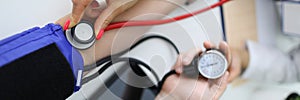 Cardiologist with red stethoscope measures blood pressure of patient in clinic closeup