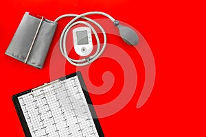 Cardiologist work desk with pulsimeter and cardiogram on red background top view copyspace