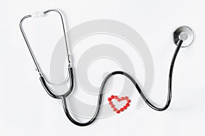 Cardiovascular system. Stethoscope and red pills in a heart shape on white background. Copy space.
