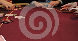 Cards and chips on the table in a casino. Close-up of hands.. Close-up of hands playing poker with chips on red table.