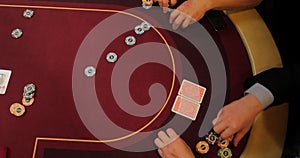 Cards and chips on the table in a casino. Close-up of hands.. Close-up of hands playing poker with chips on red table.