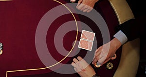 Cards and chips on the table in a casino. Close-up of hands.. Close-up of hands playing poker with chips on red table.