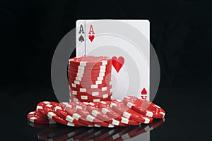 Cards of the highest denomination for the game of poker, on a black background with a reflection, along with red chips