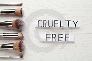 Cards with text Cruelty Free and makeup brushes on white wooden table, flat lay. Stop animal tests