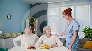 care and assistance to pensioners, a female social worker in a medical uniform helps an elderly couple and puts lunch on