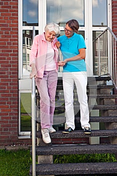 Care assistant helping a senior lady on steps.