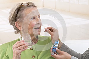 Care giver or nurse giving to elderly woman her pills