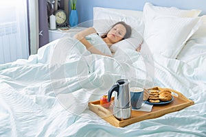 Happy young woman lying and sleep at the bed with breakfast on tray