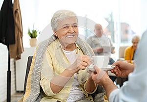 Care worker giving drink to elderly woman in hospice