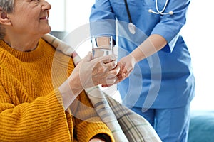 Care worker giving water to elderly woman in geriatric hospice