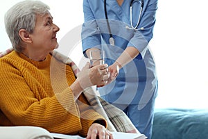 Care worker giving water to elderly woman in hospice