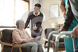 Care worker giving water to elderly woman with tablet in hospice