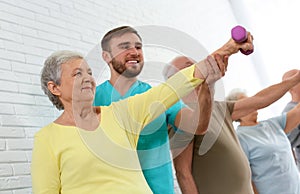 Care worker helping elderly woman to do exercise with dumbbell in gym