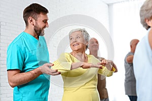 Care worker helping elderly woman to do sports exercise in gym