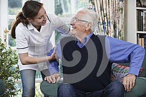 Care Worker Helping Senior Man To Get Up Out Of Chair