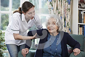 Care Worker Helping Senior Woman To Get Up Out Of Chair