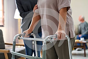 Care worker helping to elderly woman with walker in geriatric hospice