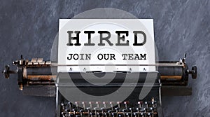 Career and employment concept. Phrase HIRED, JOIN OUR TEAM on paper sheet in vintage typewriter, grey background