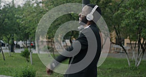 Carefree African American man walking in city singing listening to music with headphones and dancing having fun