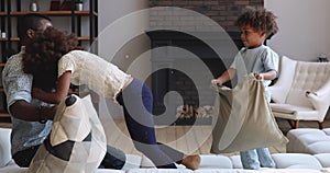 Carefree african dad and kids playing pillow fight on couch
