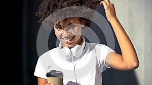 Carefree afro-american female holding cup of tea and smiling into camera, flirt