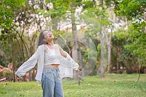 A carefree Asian woman stands with her arms outstretched, embracing the serenity of nature in a park