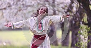 Carefree beautiful happy girl run and enjoy blooming spring trees in apple orchard. Bulgarian woman with traditional dress.