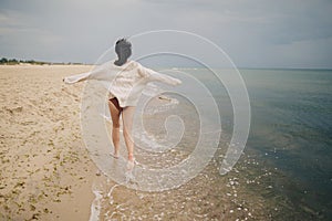 Carefree beautiful woman in knitted sweater and with windy hair running on sandy beach at cold sea, having fun. Stylish young