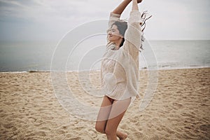 Carefree beautiful woman with windy hair running on sandy beach at cold sea waves, having fun. Stylish young happy female in