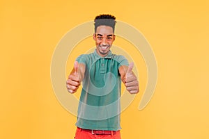 Carefree black man in casual green t-shirt smiling in studio. Indoor photo of emotional african guy