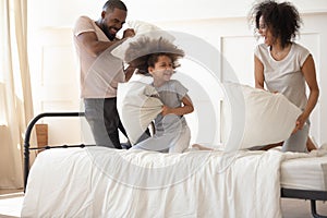 Carefree black parents small kid enjoying pillow fight on bed