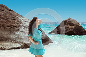 Carefree brunette woman in blue dress enjoying life near seashore in tropical beach with rocks. Enjoyment. Lifestyle. Freedom.