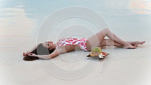 Carefree brunette woman lying on white sand Enjoying life on Tropical Beach. Sexy bikini model with exotic fruits