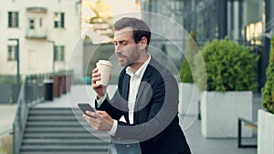 Carefree businessman drinking takeaway coffee and web surfing on smartphone, enjoying break outdoors, empty space