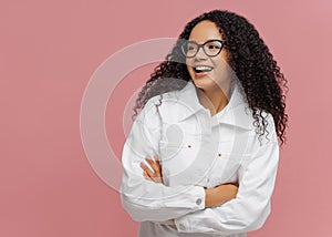 Carefree cheerful Afro American woman wears white jacket, keeps arm folded, looks aside, has charming smile, enjoys nice day in