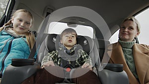 Carefree cheerful company rides in the back seat of the car. Mother with two children