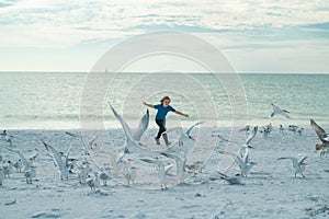 Carefree child. Child chasing birds near summer beach. Excited boy running on the beach with flying seagulls birds.