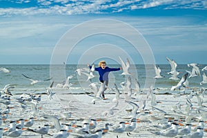 Carefree child. Child and seagull on the beach. Amazed boy running on the beach with his hands raised up with flying