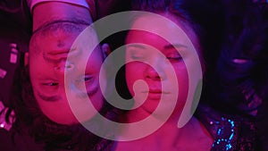 Carefree couple relaxing at rave party lying on floor top view, lights flashing
