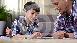 Carefree father and son playing board game, lying on floor, happy family concept