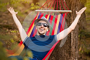 Carefree and free man raising his arms surrounded of forest nature while rest on hammock