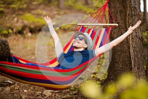 Carefree and free man raising his arms surrounded of forest nature while rest on hammock