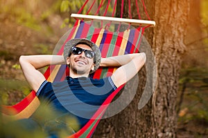 Carefree and free man raising his arms surrounded of forest nature while rest on hammock