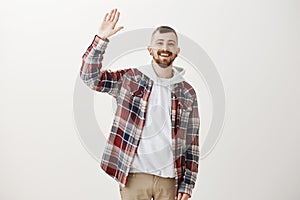 Carefree friendly male student in stylish clothes, raising palm to give high five, greeting best friend or waving