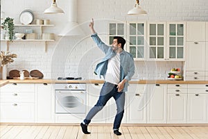 Carefree funny young man having fun dancing alone in kitchen