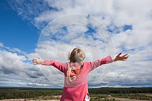 Carefree girl child with hands up against sky clouds outdoors