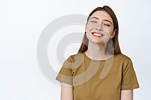 Carefree girl smiles with whitened, white teeth and closed eyes, dreaming of something with happy face expression, white