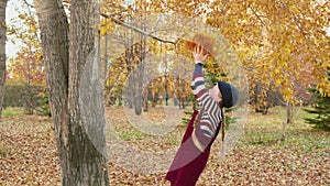 Carefree girl throwing yellow maple bouquet in autumn park. Smiling girl catching bouquet from fallen leaves in autumn