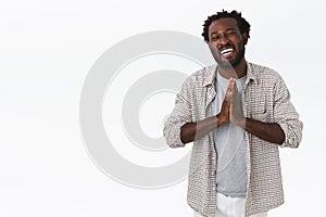 Carefree, happy and grateful kind african-american smiling man with beard, afro hairstyle, clasp hands together in pray