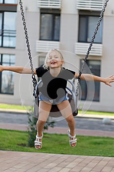 Carefree and happy little girl rides on a swing in the playground